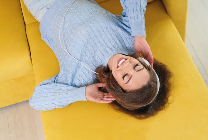 Young woman lounging on yellow couch wearing headphones